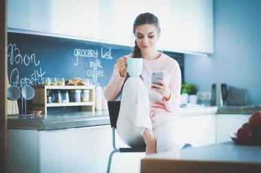 modern mutfakta otururken cep telefonu kullanan kadın.