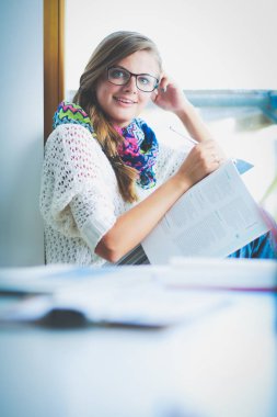 Kitapların arasında bir masada oturan genç bir kadın. Öğrenci