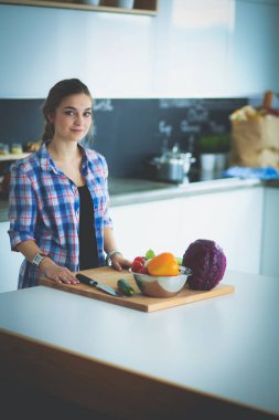 Masanın yanındaki mutfakta sebze doğrayan genç bir kadın..