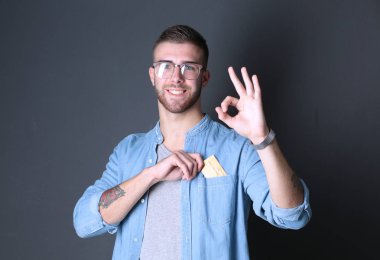 Gri arka plan üzerinde bir kredi kartı ayakta tutan genç adam. Sen