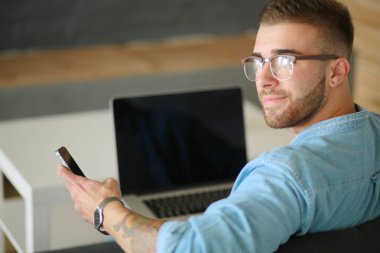 Genç bir telefonu kullanarak ve bir dizüstü bilgisayarda çalışan adam. Öğrenci manifatura