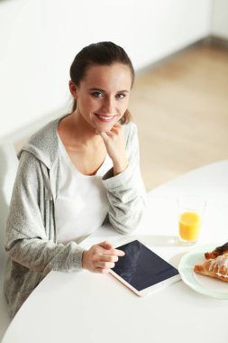 Mutfakta portakal suyu ve tableti olan genç bir kadın..