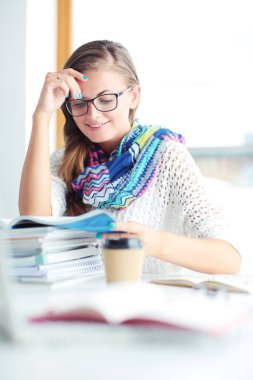 Kitapların arasında bir masada oturan genç bir kadın. Öğrenci