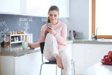 modern mutfakta otururken cep telefonu kullanan kadın.