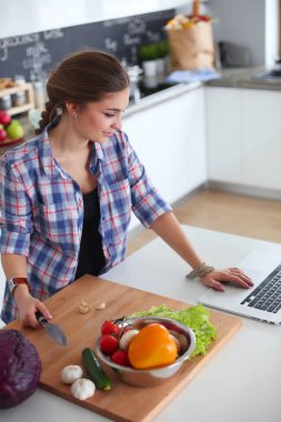 Masanın yanındaki mutfakta sebze doğrayan genç bir kadın..