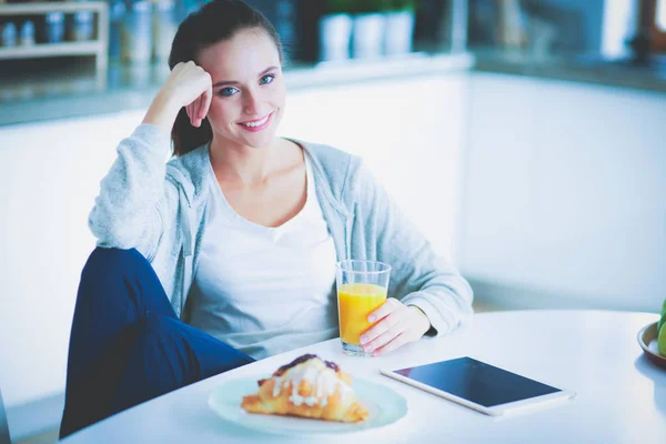 Ung kvinna med apelsinjuice och tablett i köket. — Stockfoto