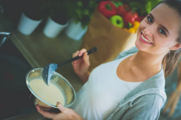 Jeune femme prépare des crêpes dans la cuisine tout en se tenant près de la table. Femme dans la cuisine. Cuisiner à la cuisine. — Photo