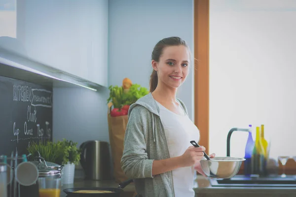 Mujer joven prepara panqueques en la cocina mientras está de pie cerca de la mesa. Mujer en la cocina. Cocinar en la cocina. — Foto de Stock