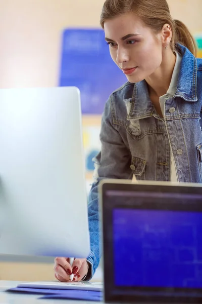 Fiatal nő áll íróasztal mellett eszközökkel, terv és laptop. — Stock Fotó
