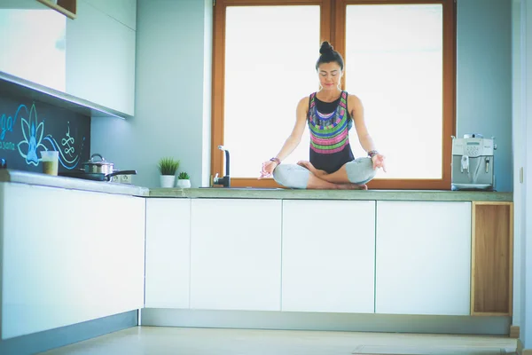 Joven hermosa mujer sentada en la mesa de la cocina en la posición de loto. Una mujer. Yoga — Foto de Stock