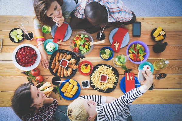 Vista superior do grupo de pessoas que jantam juntas enquanto estão sentadas à mesa de madeira. Comida na mesa. As pessoas comem fast food. — Fotografia de Stock