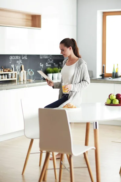 Mujer joven con jugo de naranja y tableta en la cocina. — Foto de Stock