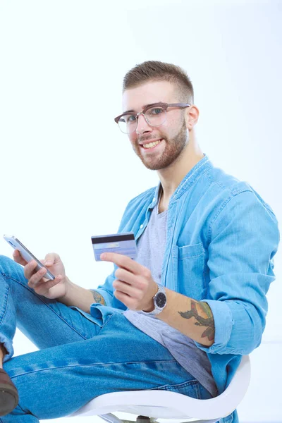 Junger Mann sitzt auf Stuhl und hält Kreditkarte. Startupper. — Stockfoto