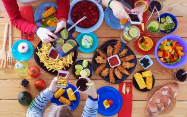 Ahşap masada otururken birlikte yemek yiyen bir grup insanın üst düzey görüntüsü. Masada yemek var. İnsanlar fast food yiyor..