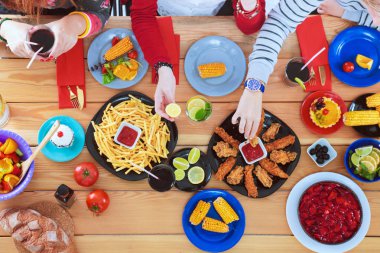 Ahşap masada otururken birlikte yemek yiyen bir grup insanın üst düzey görüntüsü. Masada yemek var. İnsanlar fast food yiyor..