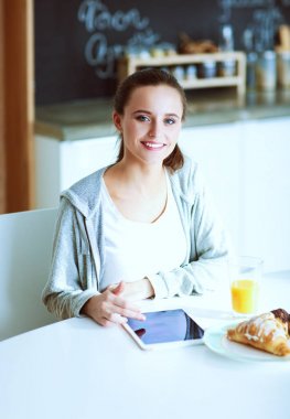 Mutfakta portakal suyu ve tableti olan genç bir kadın..