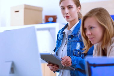 Masanın yanında duran iki genç kadın enstrüman, plan ve dizüstü bilgisayarla.