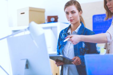 Masanın yanında duran iki genç kadın enstrüman, plan ve dizüstü bilgisayarla.