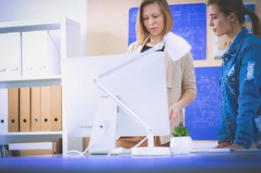 Masanın yanında duran iki genç kadın enstrüman, plan ve dizüstü bilgisayarla.