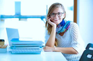 Kitapların arasında bir masada oturan genç bir kadın. Öğrenci