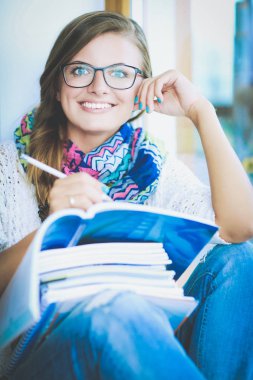 Kitapların arasında bir masada oturan genç bir kadın. Öğrenci