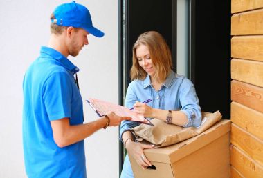Mavi üniformalı gülümseyen kurye servis konseptine paket kutusu teslim eden teslimatçı.