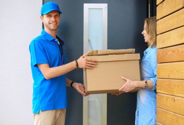 Mavi üniformalı gülümseyen kurye servis konseptine paket kutusu teslim eden teslimatçı.