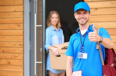 Mavi üniformalı gülümseyen kurye servis konseptine paket kutusu teslim eden teslimatçı.