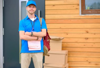 Mavi üniformalı gülümseyen kurye servis konseptine paket kutusu teslim eden teslimatçı.