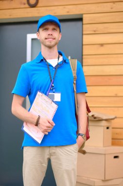 Mavi üniformalı gülümseyen kurye servis konseptine paket kutusu teslim eden teslimatçı.