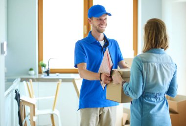 Mavi üniformalı gülümseyen kurye servis konseptine paket kutusu teslim eden teslimatçı.
