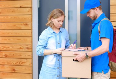 Mavi üniformalı gülümseyen kurye servis konseptine paket kutusu teslim eden teslimatçı.