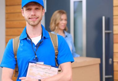 Mavi üniformalı gülümseyen kurye servis konseptine paket kutusu teslim eden teslimatçı.