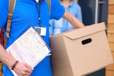 Mavi üniformalı gülümseyen kurye servis konseptine paket kutusu teslim eden teslimatçı.