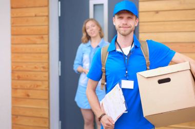 Mavi üniformalı gülümseyen kurye servis konseptine paket kutusu teslim eden teslimatçı.