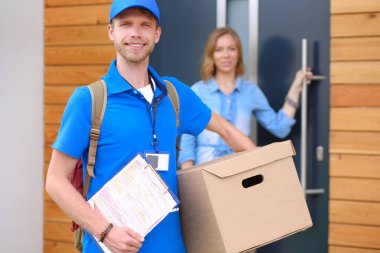 Mavi üniformalı gülümseyen kurye servis konseptine paket kutusu teslim eden teslimatçı.