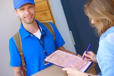 Mavi üniformalı gülümseyen kurye servis konseptine paket kutusu teslim eden teslimatçı.