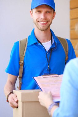 Mavi üniformalı gülümseyen kurye servis konseptine paket kutusu teslim eden teslimatçı.