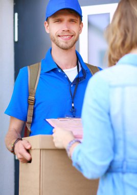 Mavi üniformalı gülümseyen kurye servis konseptine paket kutusu teslim eden teslimatçı.