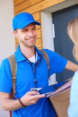 Mavi üniformalı gülümseyen kurye servis konseptine paket kutusu teslim eden teslimatçı.