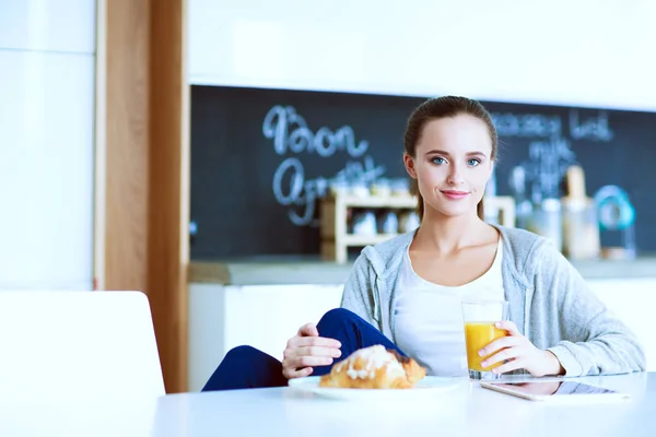 Ung kvinna med apelsinjuice och tablett i köket. — Stockfoto