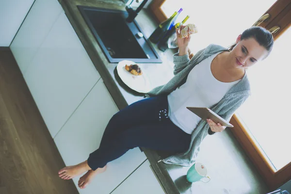 Hermosa joven usando una tableta digital en la cocina. — Foto de Stock