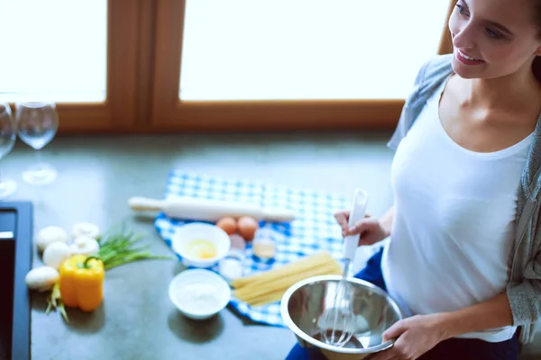 Jovem prepara panquecas na cozinha enquanto está perto da mesa. Uma mulher na cozinha. Cozinhar na cozinha. — Fotografia de Stock