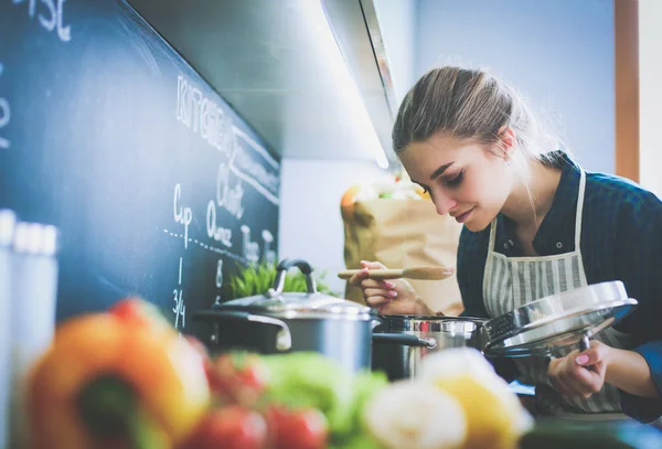 Mujer joven parada junto a la estufa en la cocina . — Foto de Stock