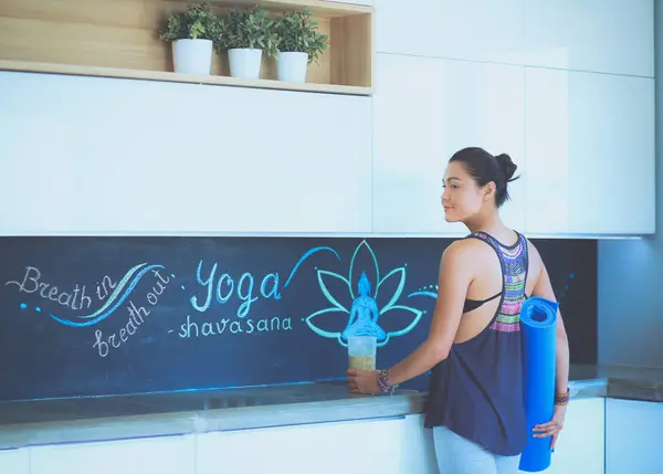 Retrato de una mujer sonriente sosteniendo en su mano una esterilla de yoga mientras estaba de pie en el estudio. Yoga. Una mujer. Bienestar — Foto de Stock