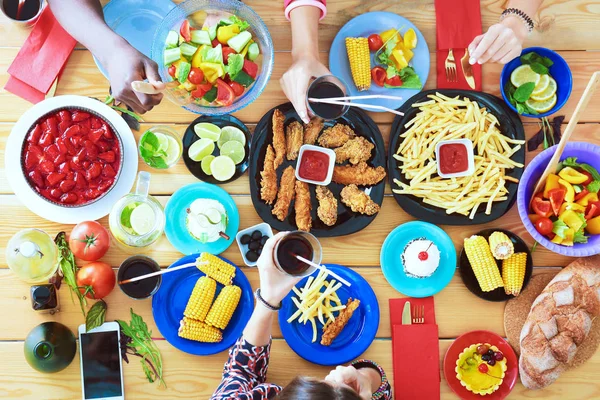 Vue du dessus du groupe de personnes qui dînent ensemble tout en étant assis à une table en bois. De la nourriture sur la table. Les gens mangent fast food. — Photo