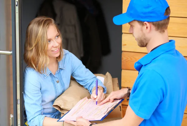 Repartidor sonriente en uniforme azul que entrega la caja de paquetes al destinatario - concepto de servicio de mensajería — Foto de Stock