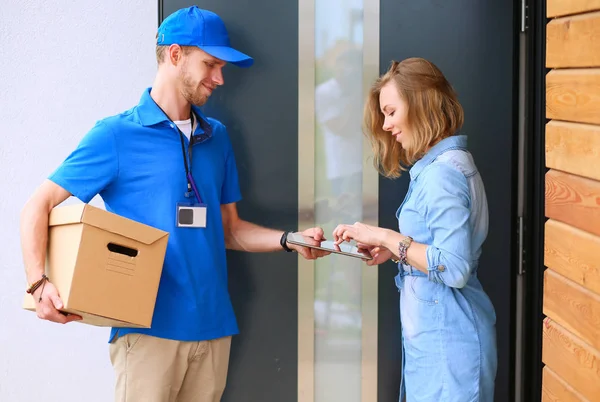 Uomo di consegna sorridente in uniforme blu che consegna pacchi al destinatario - concetto di servizio di corriere — Foto Stock