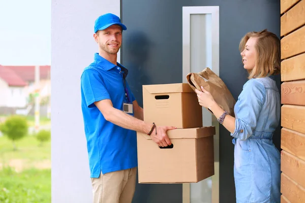 Pria pengantar senyum dengan seragam biru mengantarkan kotak paket ke penerima - konsep layanan kurir — Stok Foto