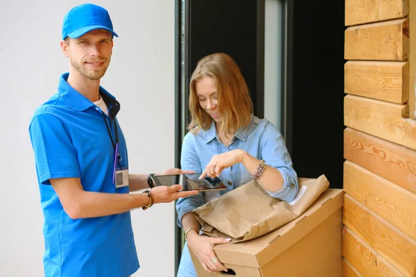 Χαμογελαστή παράδοση άνθρωπος σε μπλε στολή παράδοση δεμάτων κουτί στον παραλήπτη - έννοια της υπηρεσίας ταχυμεταφορών — Φωτογραφία Αρχείου